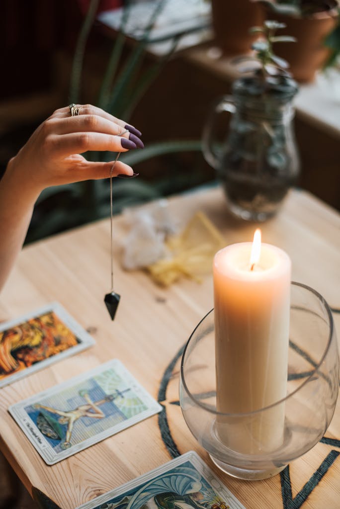 Crop soothsayer with talisman and tarot cards near glowing candle