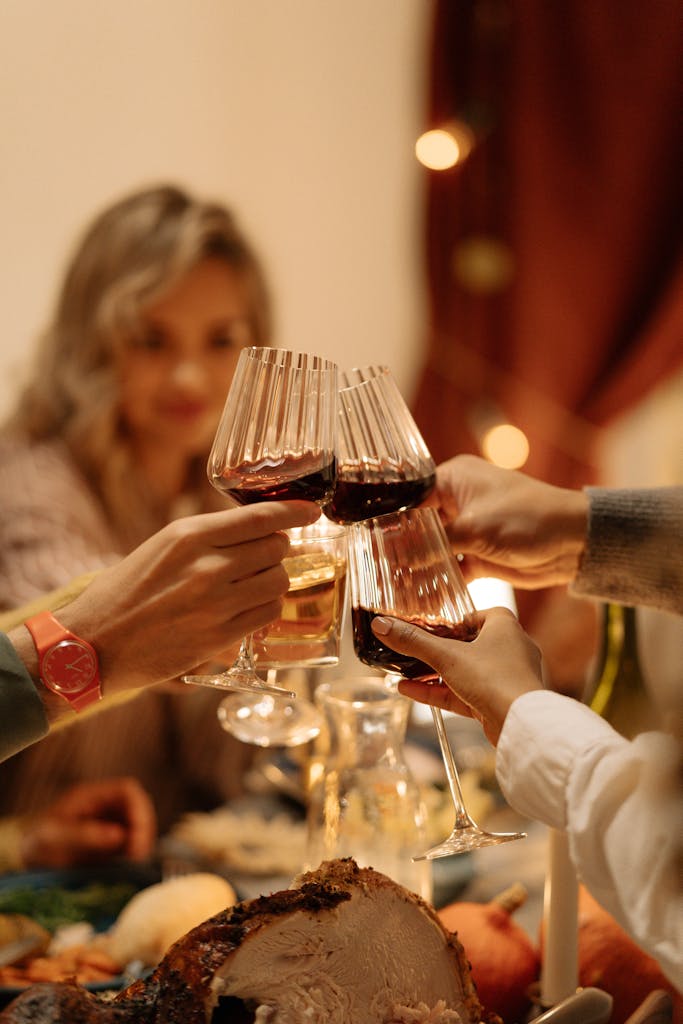 Close-up of friends toasting with wine glasses during a festive dinner indoors.